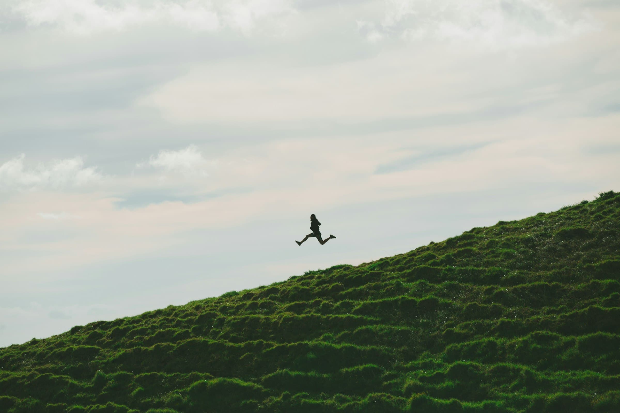 Silhouette of an athlete leaping up a grassy hill